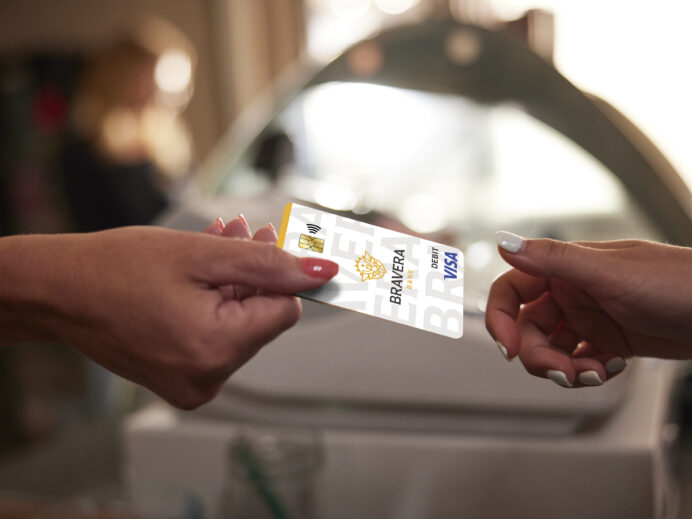 A close-up up a person handing a Bravera Visa card to a customer