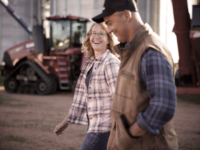 An image from the Bravera marketing collateral of a man and woman wearing flannel walking together with farming equipment in the back